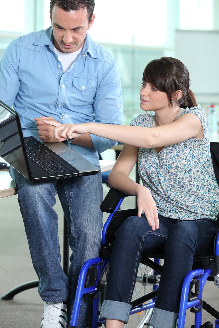 woman in wheelchair being shown something on a laptop
