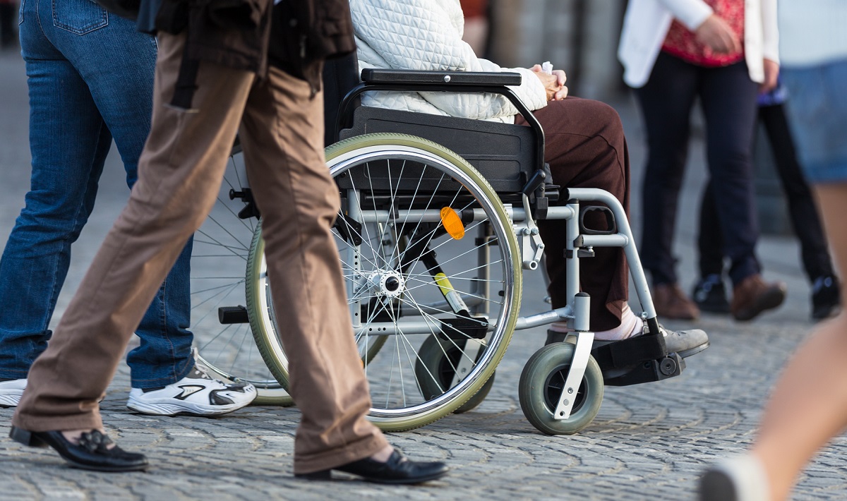 A Disabled Person On Wheelchair and other person walking around